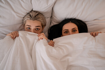 top view of young lesbian couple lying in bed under blanket