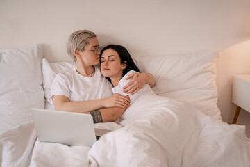 Fototapeta premium young lesbian couple hugging while lying on bed near laptop