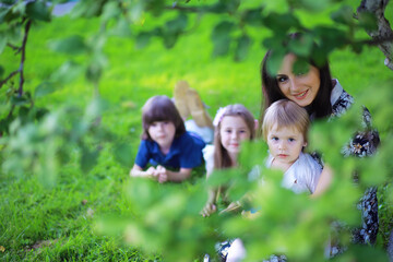Fototapeta premium Young large family on a summer morning walk. Beautiful mother with children is playing in the park.