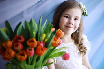 Beautiful girl in white dresses with a magnificent bouquet of the first tulips. International Women's Day. Girl with tulips.