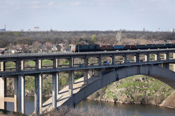 Fototapeta na wymiar View of the reinforced concrete two-level arched bridge. Freight train rides across the bridge.