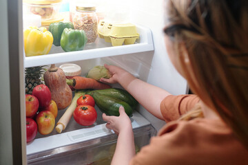 Woman taking fresh zucchini out of fridge to make healthy delicious dish for dinner