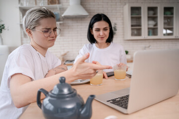 lesbian woman in glasses pointing at laptop near blurred girlfriend