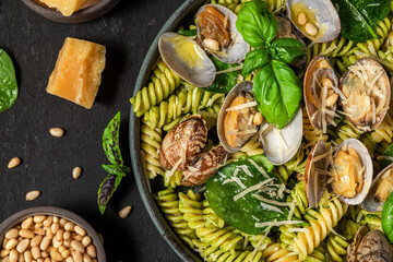 Salad made of pasta fusilli, seafood vongole, spinach, parmesan cheese and pine nut in a plate on black table. Top view