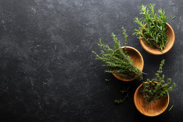 Obraz na płótnie Canvas Fresh rosemary, thyme in wooden bowls on a black background with copy space.