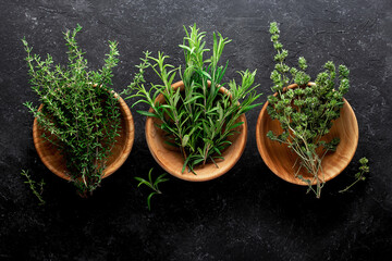 Obraz na płótnie Canvas Fresh rosemary, thyme in wooden bowls on a black background, top view.
