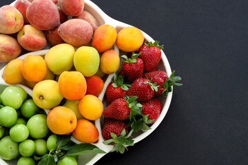 Top view of Fresh summer fruits, plum, peach, apricot, strawberry in plate on black background, copy space, food concept.