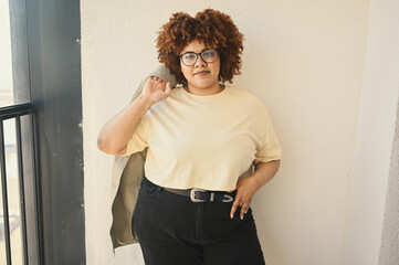 Beautiful happy smiling curvy plus size African black woman afro hair posing in beige t-shirt,...