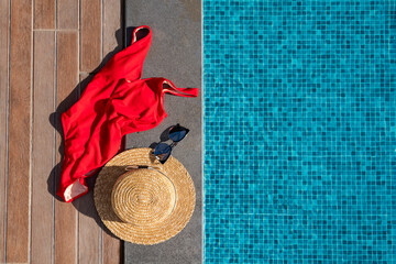 Red feminine swimsuit, straw hat and sunglasses near the swimming pool