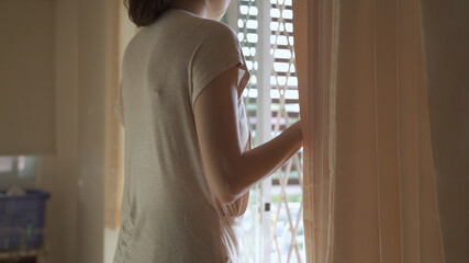 asian housewife woman closing sliding door window and pulling curtains to block sunlight at home....