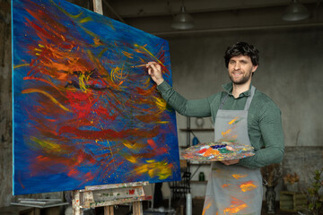 Portrait of male artist working on painting in studio. Male artist makes strokes with yellow paint