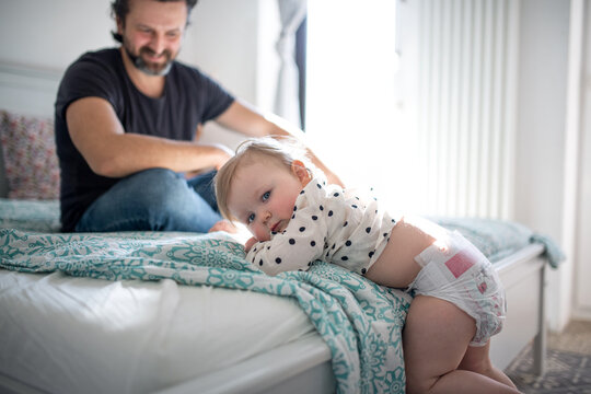 Small toddler girl with father indoors in bedroom at home, looking at camera.