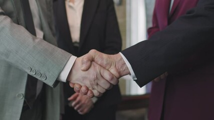 Midsection slowmo of two unrecognizable foreign affairs ministers shaking hands greeting each other before negotiations in modern conference room while their assistants standing in background