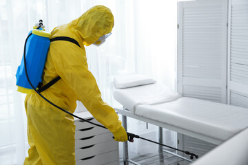 Employee in protective suit sanitizing doctor's office. Medical disinfection