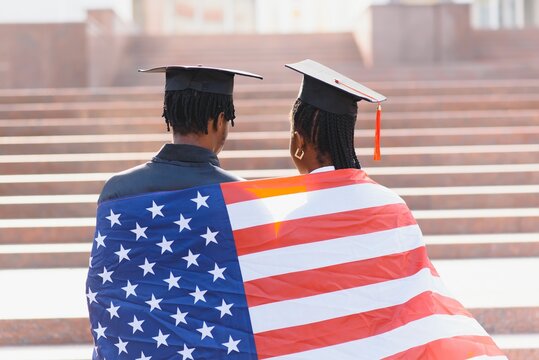 education, graduation and people concept - happy international students in mortar boards and bachelor gowns with american flag