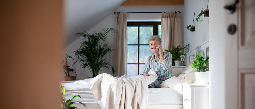 Happy senior woman using smartphone in bed at home.