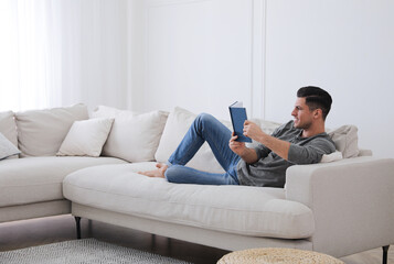 Fototapeta na wymiar Man with book lying on comfortable sofa in living room