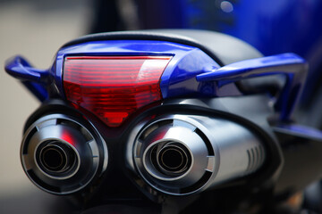 Dual motorcycle exhaust pipes on a blue bike with red taillight