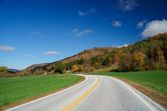 The long winding road leading towards the deep wood full of colorful foliage under the deep blue sky on a sunny autumn after in Vermont, United States 