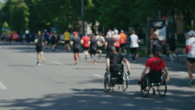 Disabled persons in wheelchairs taking park in street marathon, crowd of people running ahead of them on asphalt road. Blurred sports background. Healthy lifestyle and inspiration