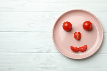 Plate with happy face made of tomato on white wooden background