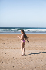 Young caucasian woman running to the sea on the beach with a pink bikini.