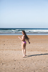 Fototapeta na wymiar Young caucasian woman running to the sea on the beach with a pink bikini.