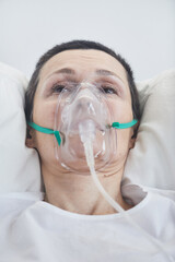 Close-up of mature woman in oxygen mask lying on hospital bed