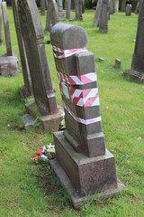 Security tape wrapped around a leaning gravestone due to vandalism in a grave yard - 434077066