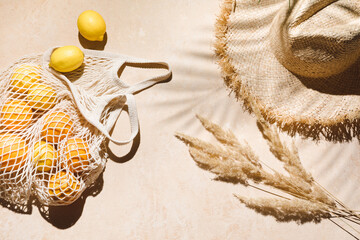 Summer flat lay on beige background. Straw hat and lemon fruits in eco friendly mesh shopping bag....