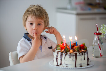 Four years old blond child, preschool boy, celebrating birthday at home with homemade cake
