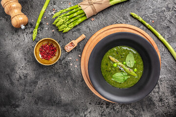 Delicious soup with asparagus in ceramic bowl, on rustic wooden background. Clean eating, dieting, vegan, vegetarian, healthy food concept. top view