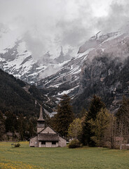 Obraz premium Old alpine church in the village of Kandersteg in Switzerland set against a misty mountain glacier background high in the alps.