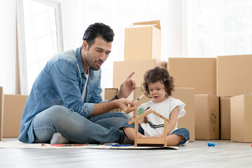 Happy Caucasian young father and little daughter enjoy coloring wooden toy house together on new home floor. Dad tease cute child by putting a paint brush and paint water color on child's face.