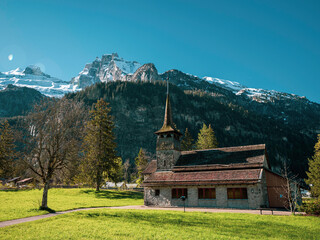 Fototapeta na wymiar Beautiful old rustic alpine church and snow capped alpine mountains. The church is situated in the alpine village of kandersteg in Switzerland.