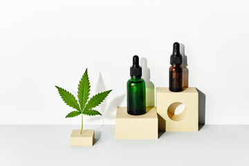 Cosmetic products with CBD oil and hemp extract. Glass bottles and hemp leaf on abstract geometric...