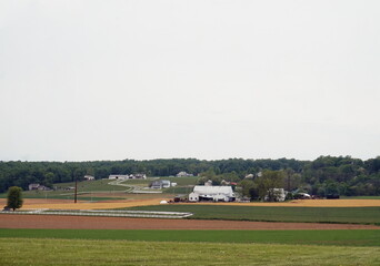 Fototapeta na wymiar Village of Homes and Farm Buildings in the Midst of Green and Plowed Farm Fields in Daylight