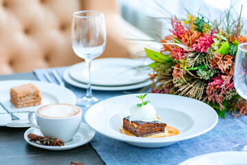 Chocolate cake with a ball of white ice cream decorated with mint leaf and caramel syrup is served on a large white plate in the restaurant. Restaurant menu.