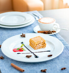 A piece of honey cake on a large white plate, decorated with chocolate syrup, mint. Restaurant menu