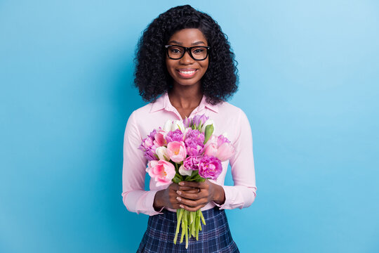 Photo portrait of smiling woman in spectacles keeping tulips bouquet in spring isolated on vivid blue color background