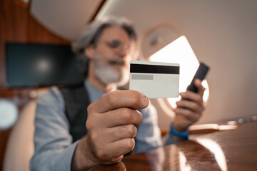 Credit card in hand of businessman using smartphone on blurred background in jet