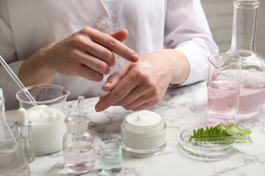 Scientist testing cosmetic product at white marble table in laboratory, closeup