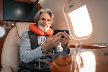 Smiling businessman in neck pillow using smartphone in plane