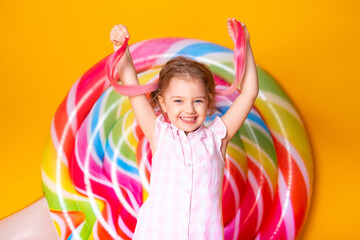 Happy excited arab child girl in colorful striped dress having fun on yellow background with lollipop