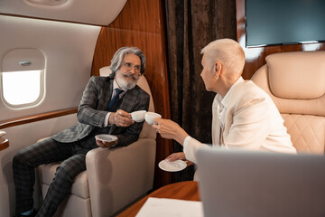 Fototapeta premium Business people clinking with coffee cups in private jet