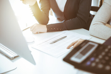 Accountant checking financial statement or counting by calculator income for tax form, hands closeup. Business woman sitting and working with colleague at the desk in office. Tax and Audit concept