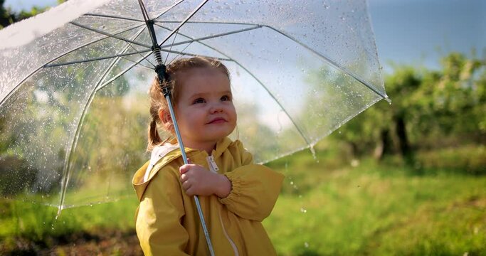cute toddler baby girl watching the rain drops falling on her umbrella in spring garden