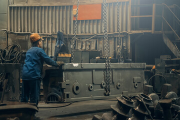 Metallurgical plant or foundry worker controls movement of large steel product being moved by crane...