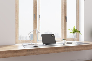 Modern home office with wooden tabletop, modern laptop, city view from the window, white coffee mug and lamp and glass vase.