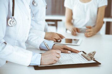 Unknown woman-doctors at work consulting patient. Female physicians filling up medical documents or prescription, close-up. Health care concept